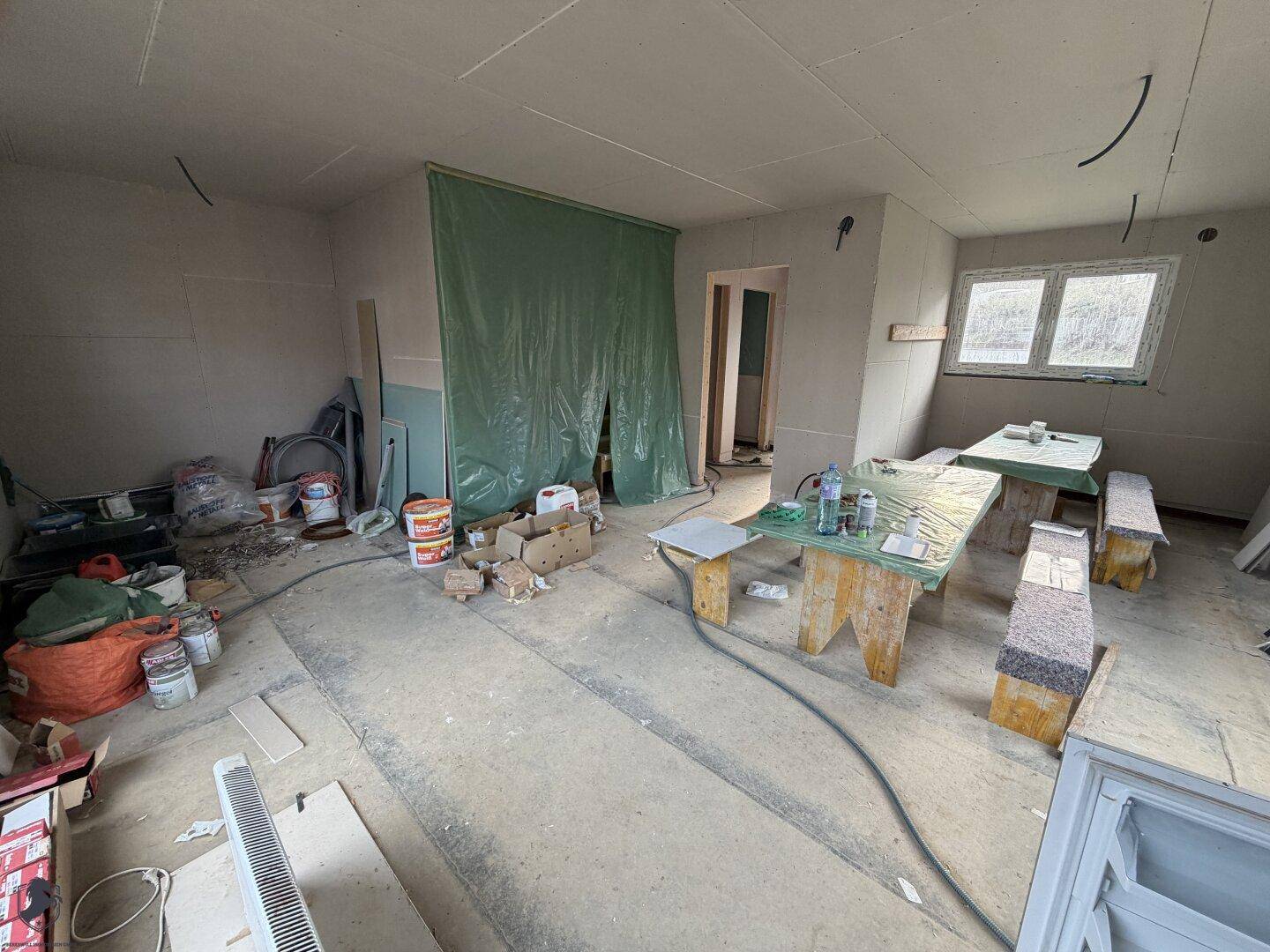 Geräumiger Wohnbereich im Rohbau mit Arbeitsflächen und Baumaterialien.