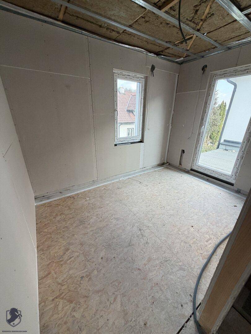 Zimmer im Rohbau mit Fenster und OSB-Plattenboden.