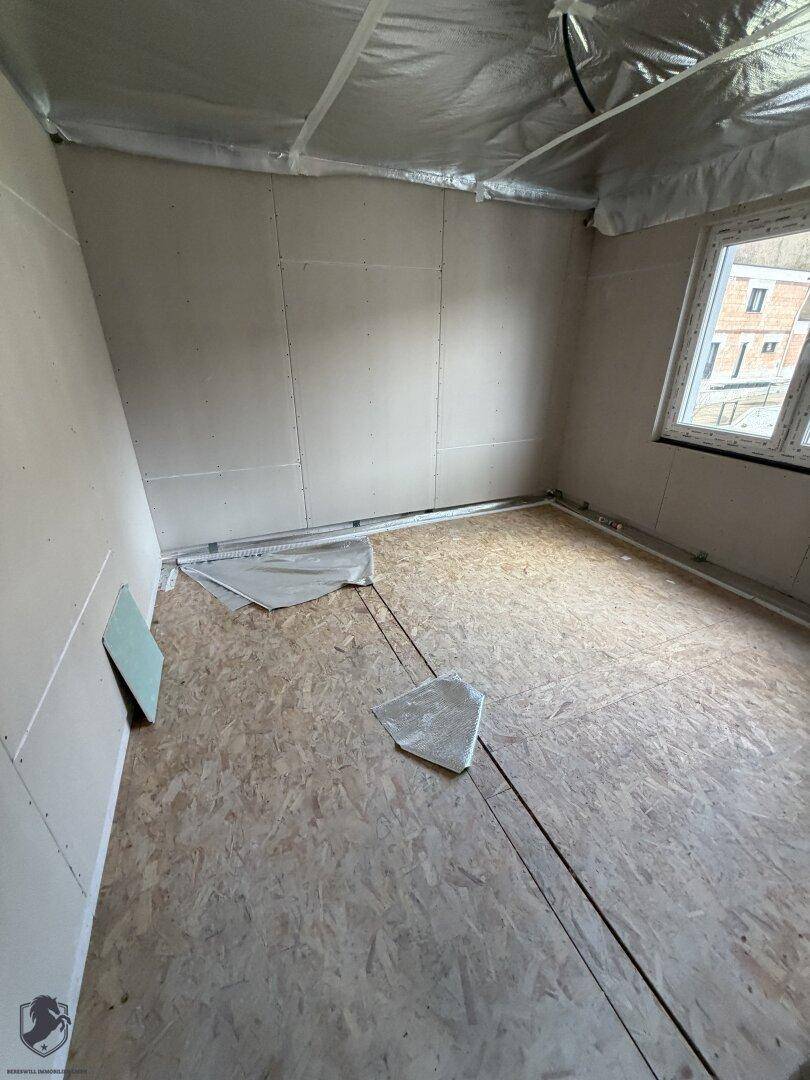 Zimmer im Rohbau mit Fenster und OSB-Plattenboden.