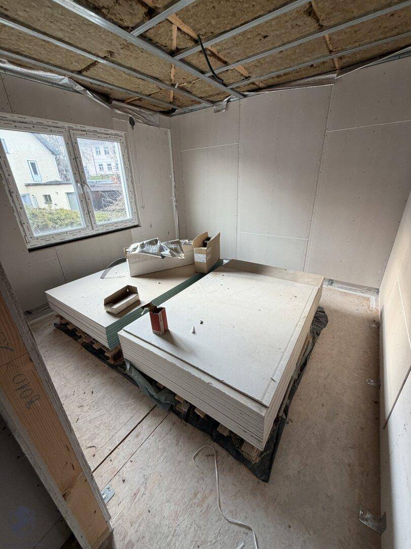 Zimmer im Rohbau mit Fenster und Baumaterialien.