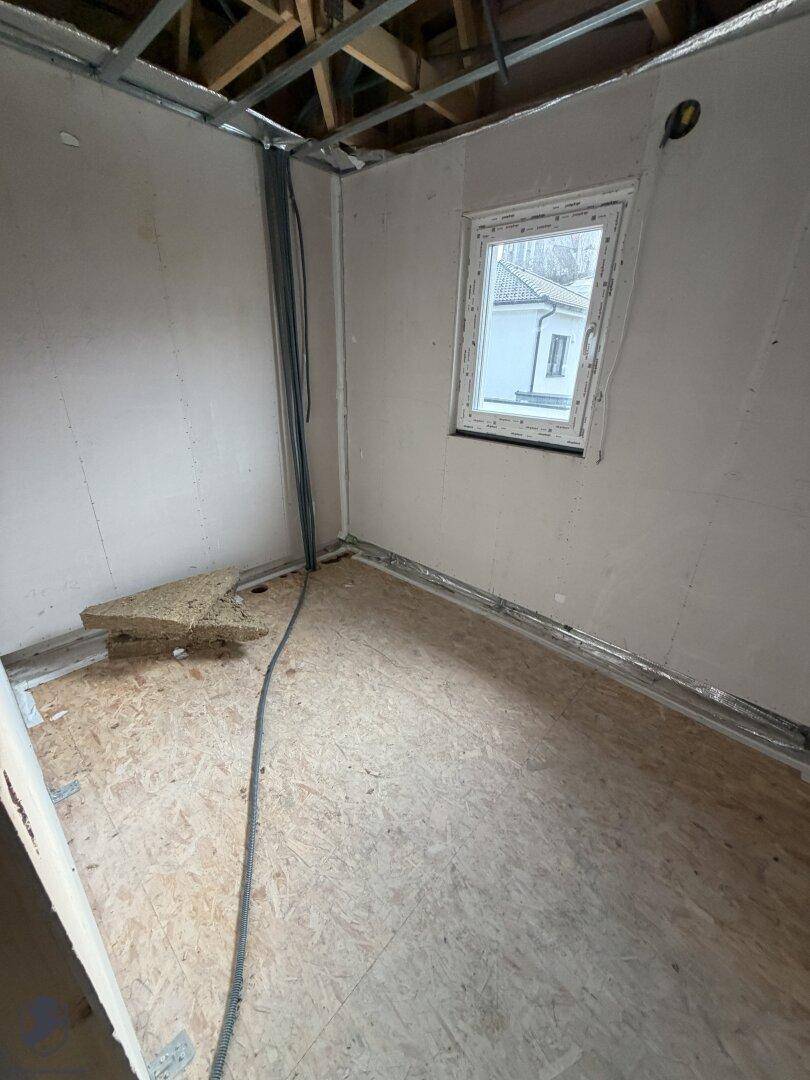 Zimmer im Rohbau mit Fenster und OSB-Plattenboden.
