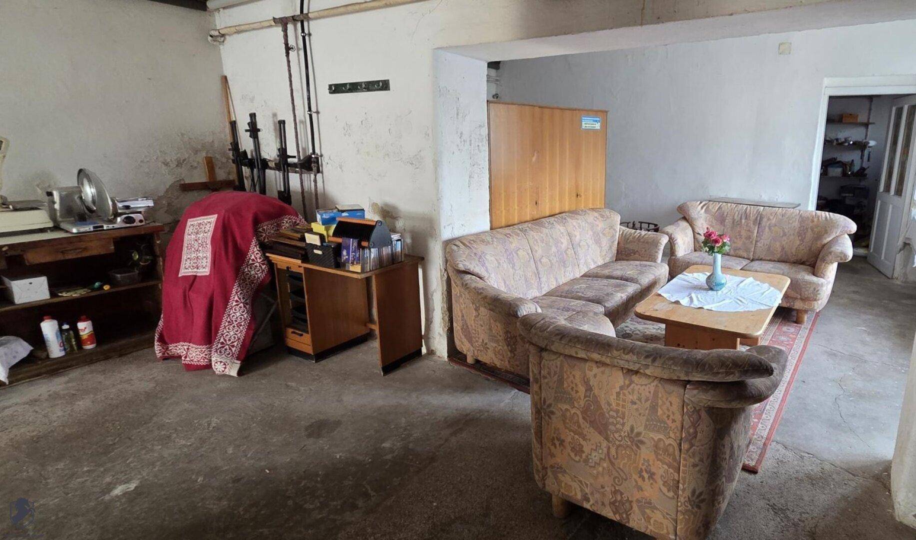 Großer Kellerraum mit Betonboden, älteren Sofas und Stauraum.
