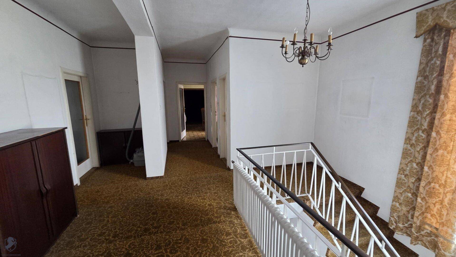 Geräumiger Flur mit Teppichboden, Treppe und klassischem Kronleuchter.