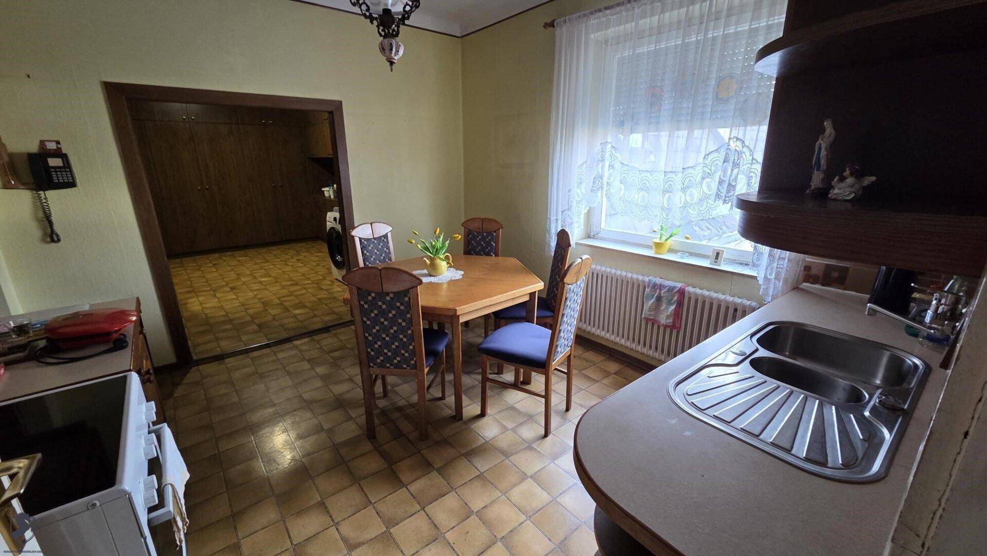 Gemütliche Wohnküche mit Esstisch, Holzschränken und Fenster.