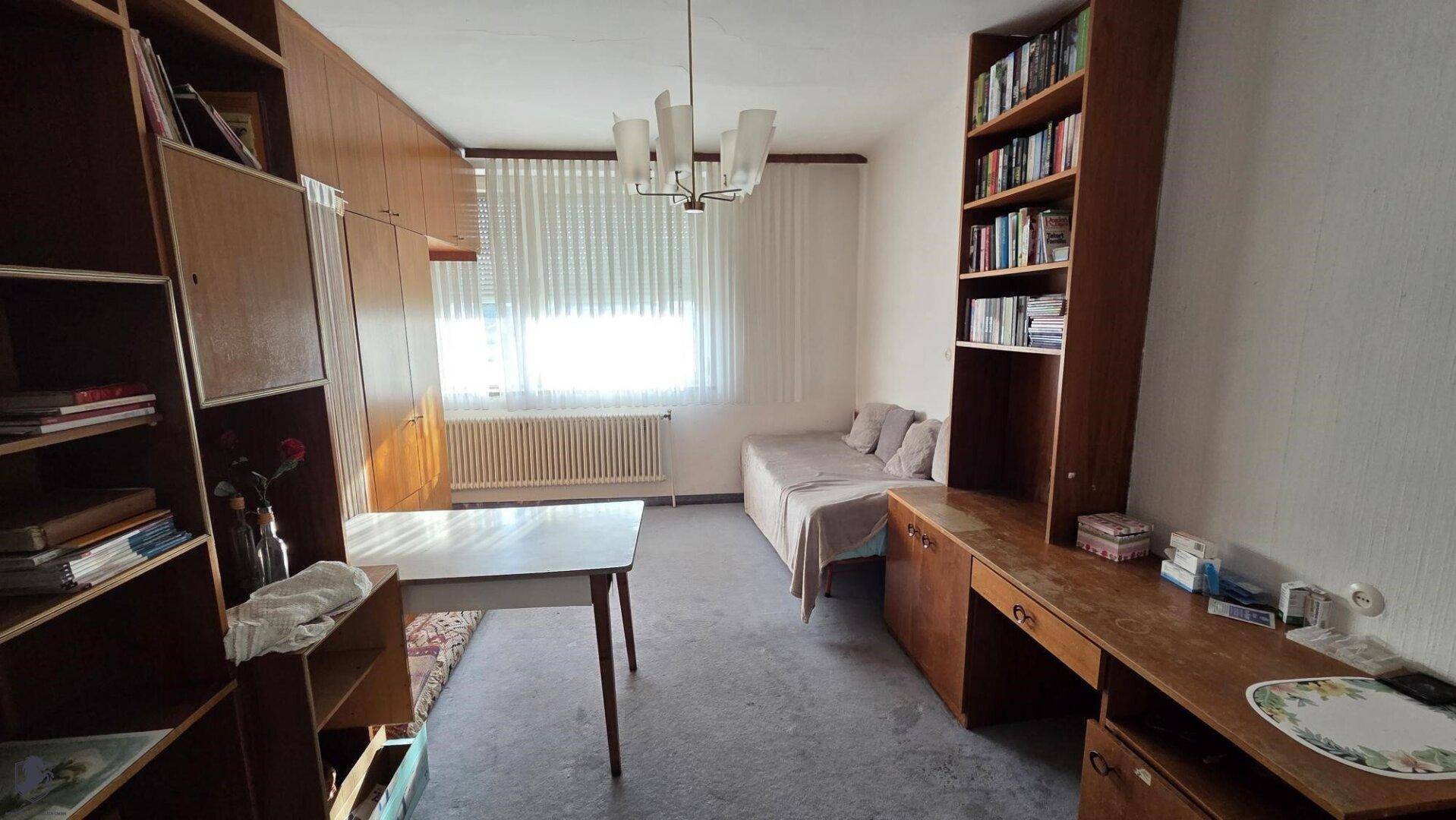 Schlafzimmer oder Arbeitszimmer mit Bett, Schreibtisch und Bücherregalen.