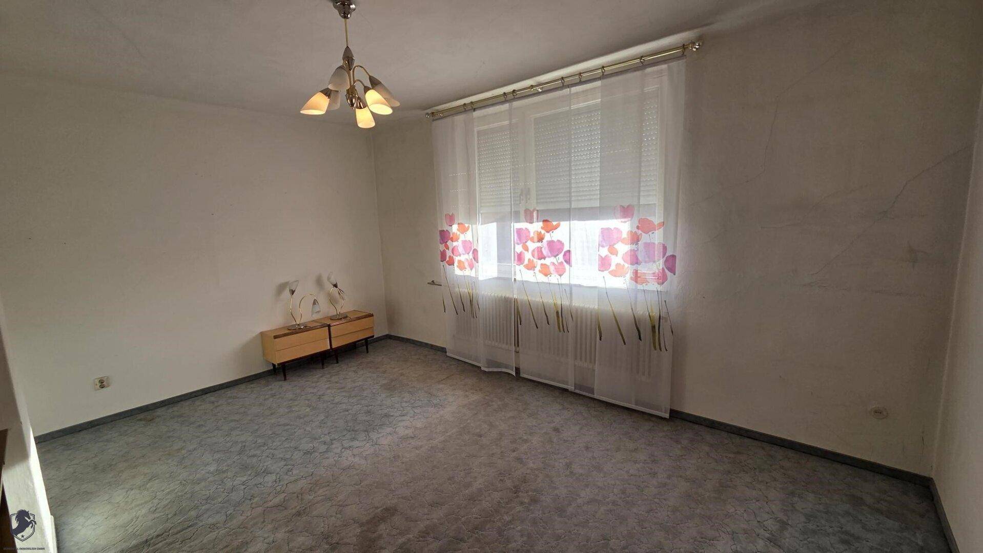 Leeres Zimmer mit Teppichboden und Fenster mit floralen Vorhängen.