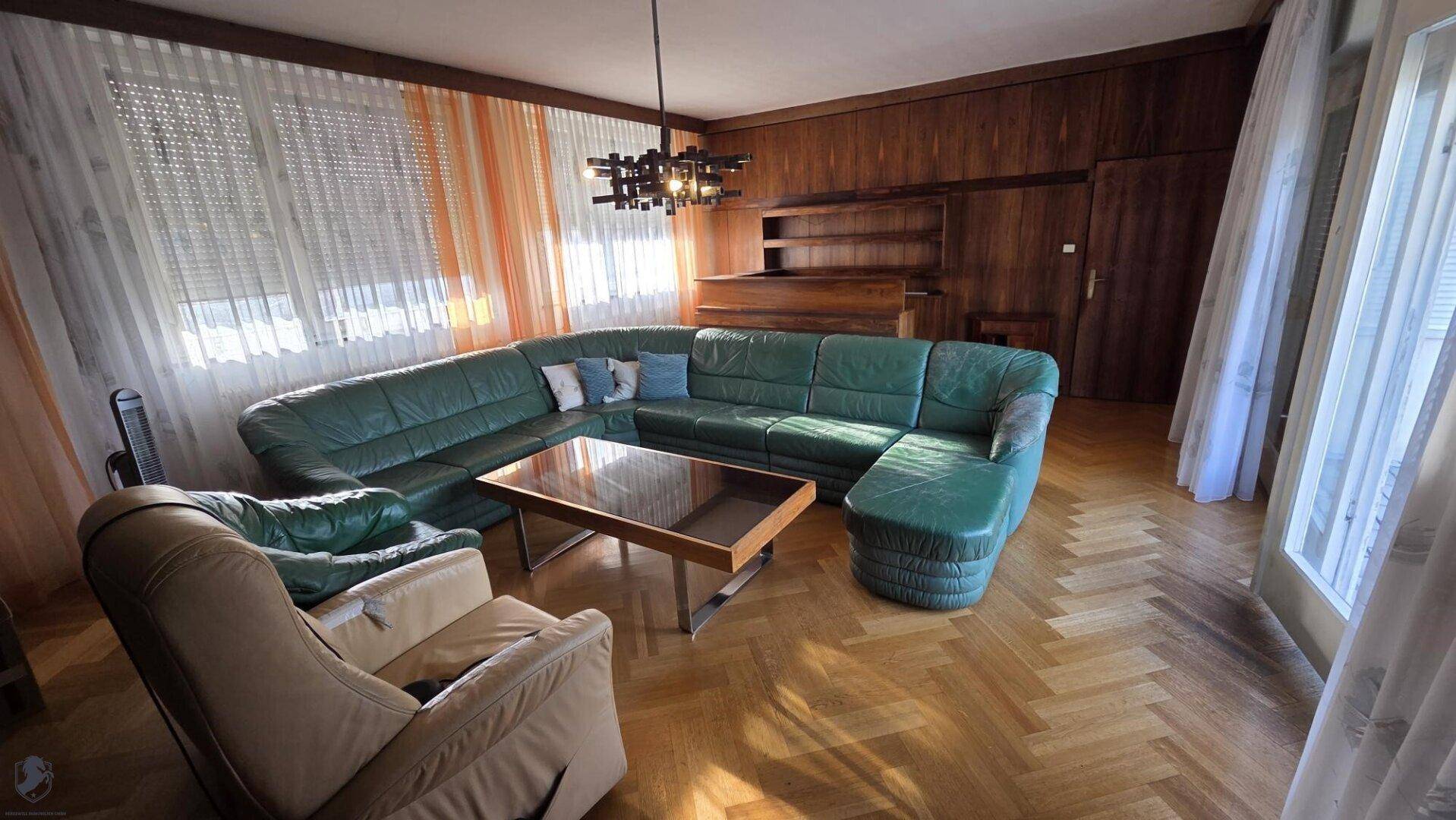 Geräumiges Wohnzimmer mit grünem Ledersofa, Parkettboden und Holzvertäfelung.