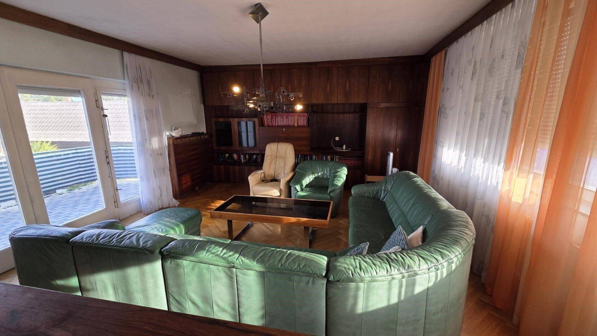 Helles Wohnzimmer mit Ledersofa, Parkett und Zugang zur Terrasse.