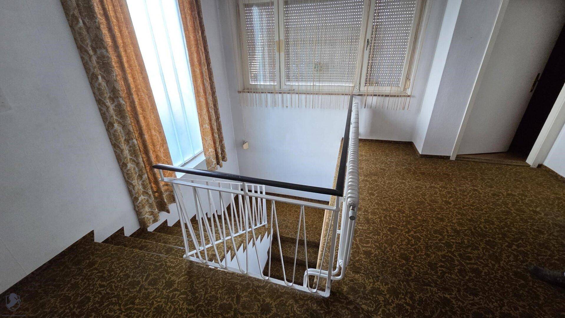 Treppenhaus mit Teppichboden, weißem Geländer und Fenster.