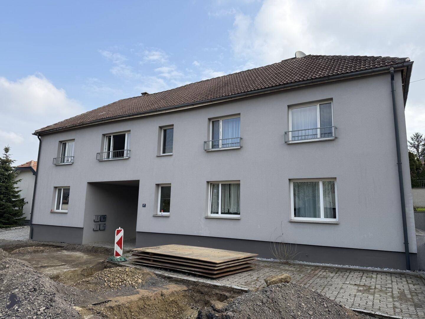 Mehrfamilienhaus mit grauer Fassade und Baustelle im Vordergrund unter bewölktem Himmel.