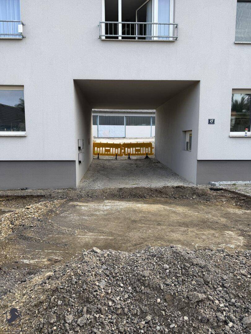 Durchgangsbereich eines Gebäudes mit Baustellenschildern und Schotterboden.