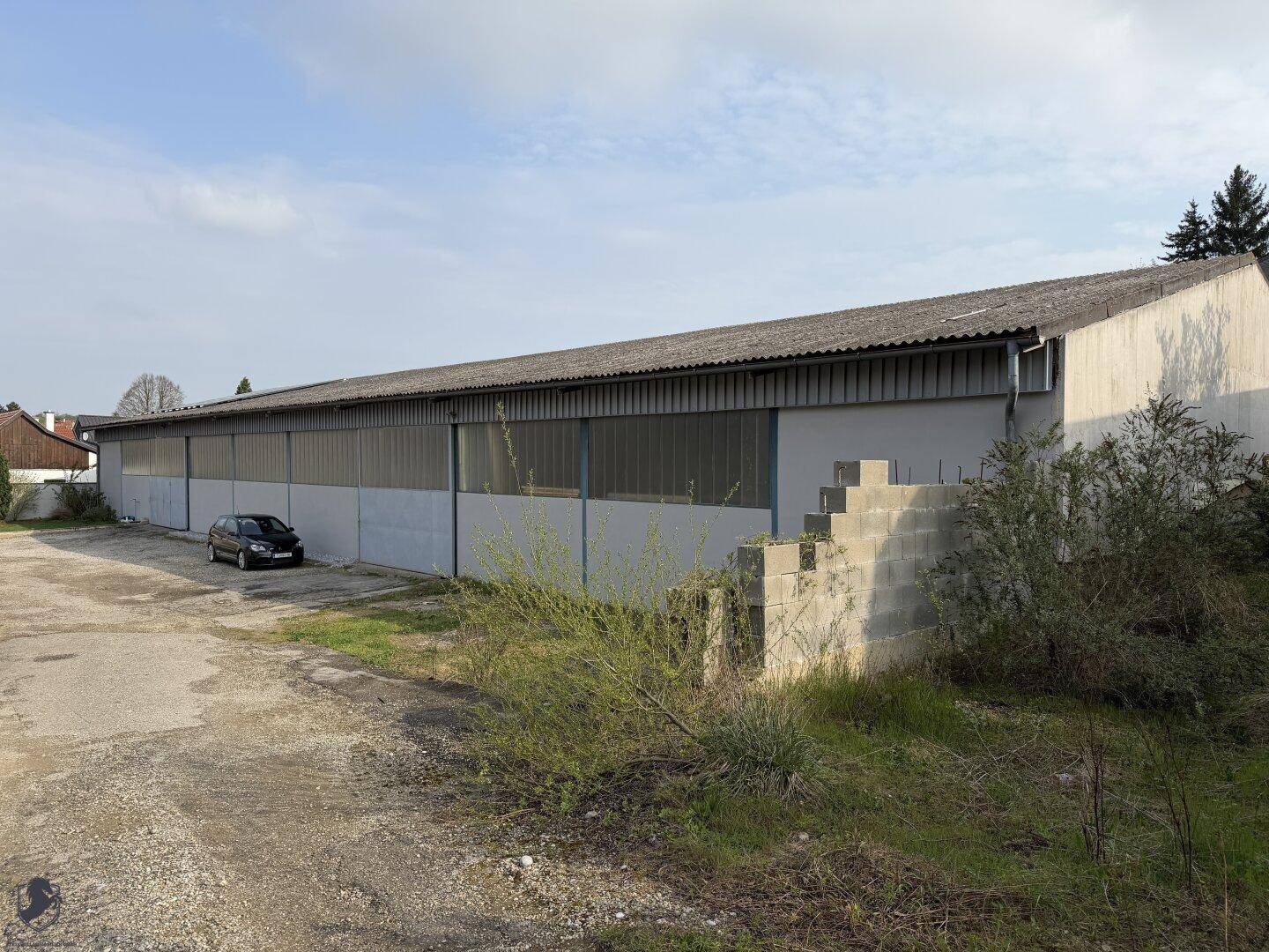 Lange, einstöckige Halle mit Wellblechdach und großem Vorplatz, umgeben von Grünflächen.