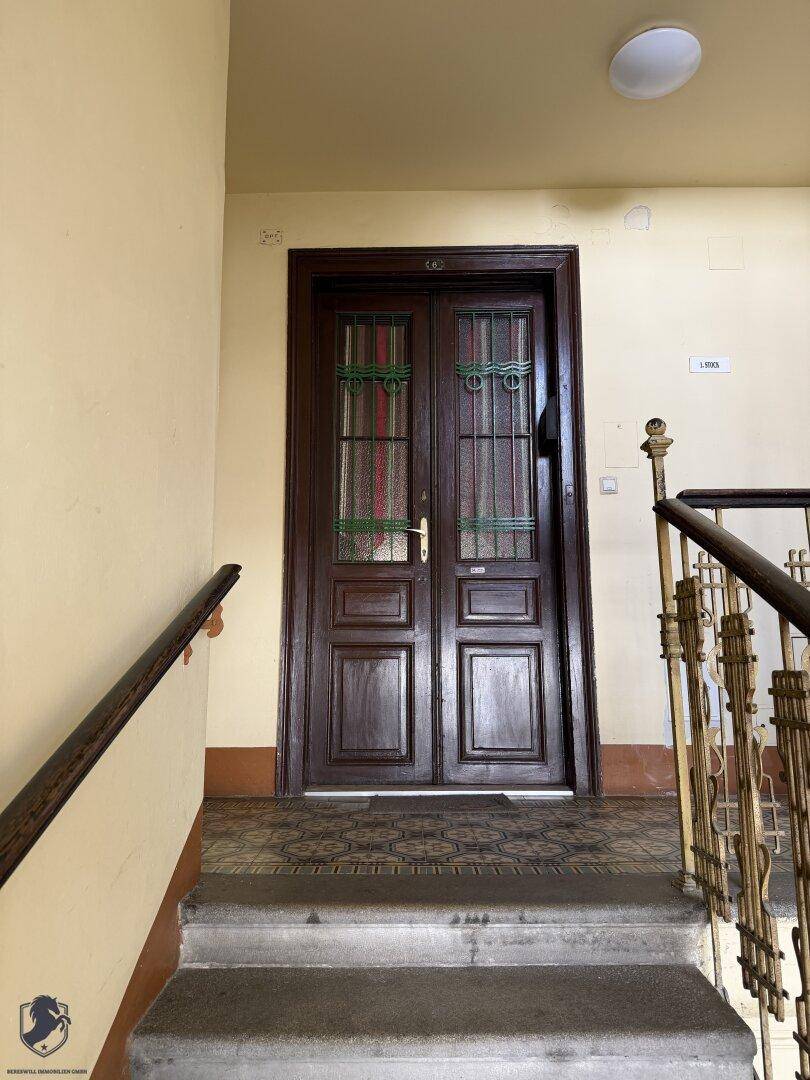 Treppenabsatz mit einer traditionellen Holztür und einem verzierten Geländer in einem Altbau.