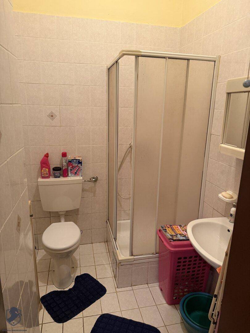 Kleines Badezimmer mit Duschkabine, WC und Waschbecken, komplett gefliest.