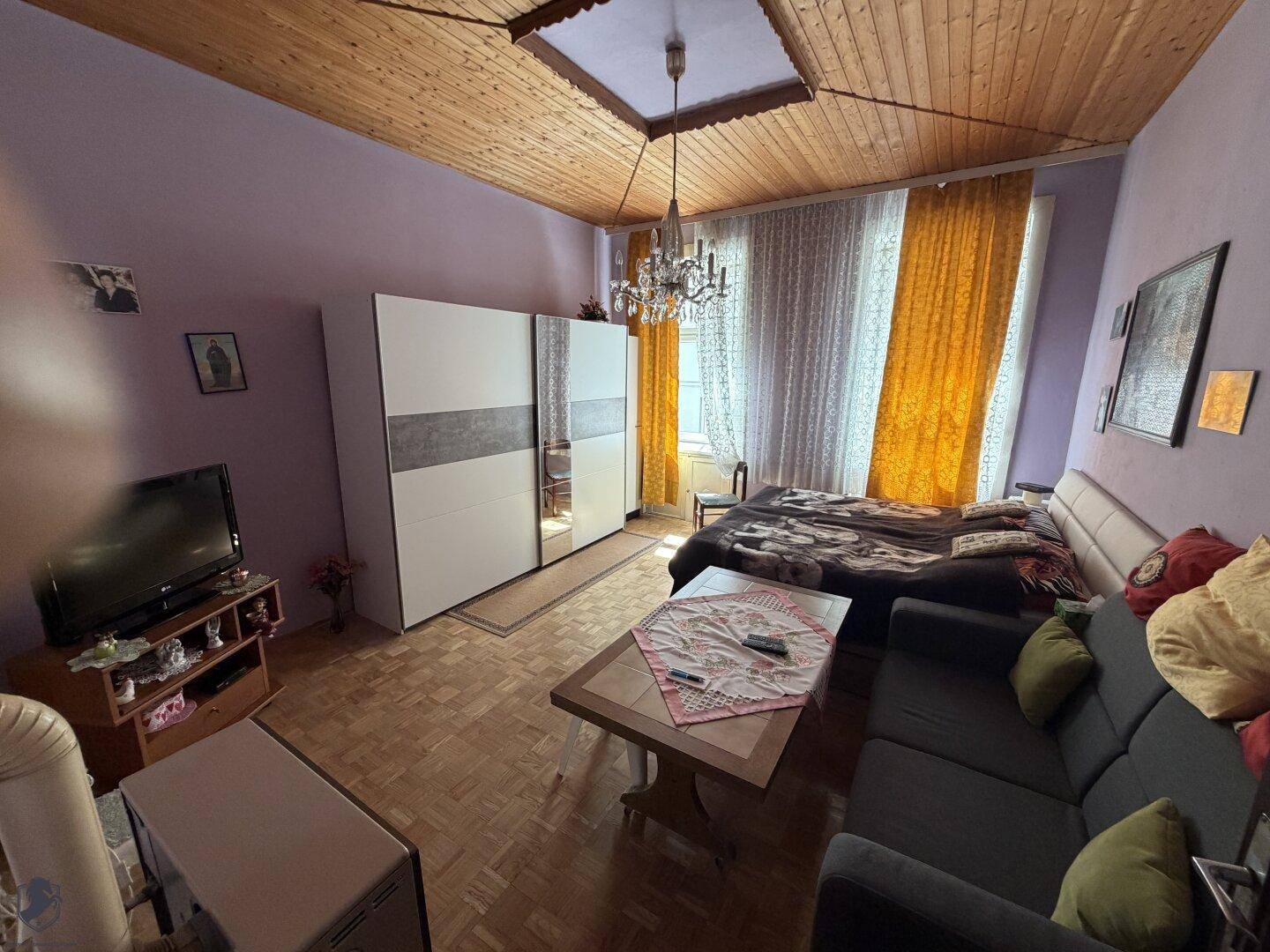 Geräumiges Zimmer mit Holzbalkendecke, Parkettboden und kombiniertem Wohn- und Schlafbereich.