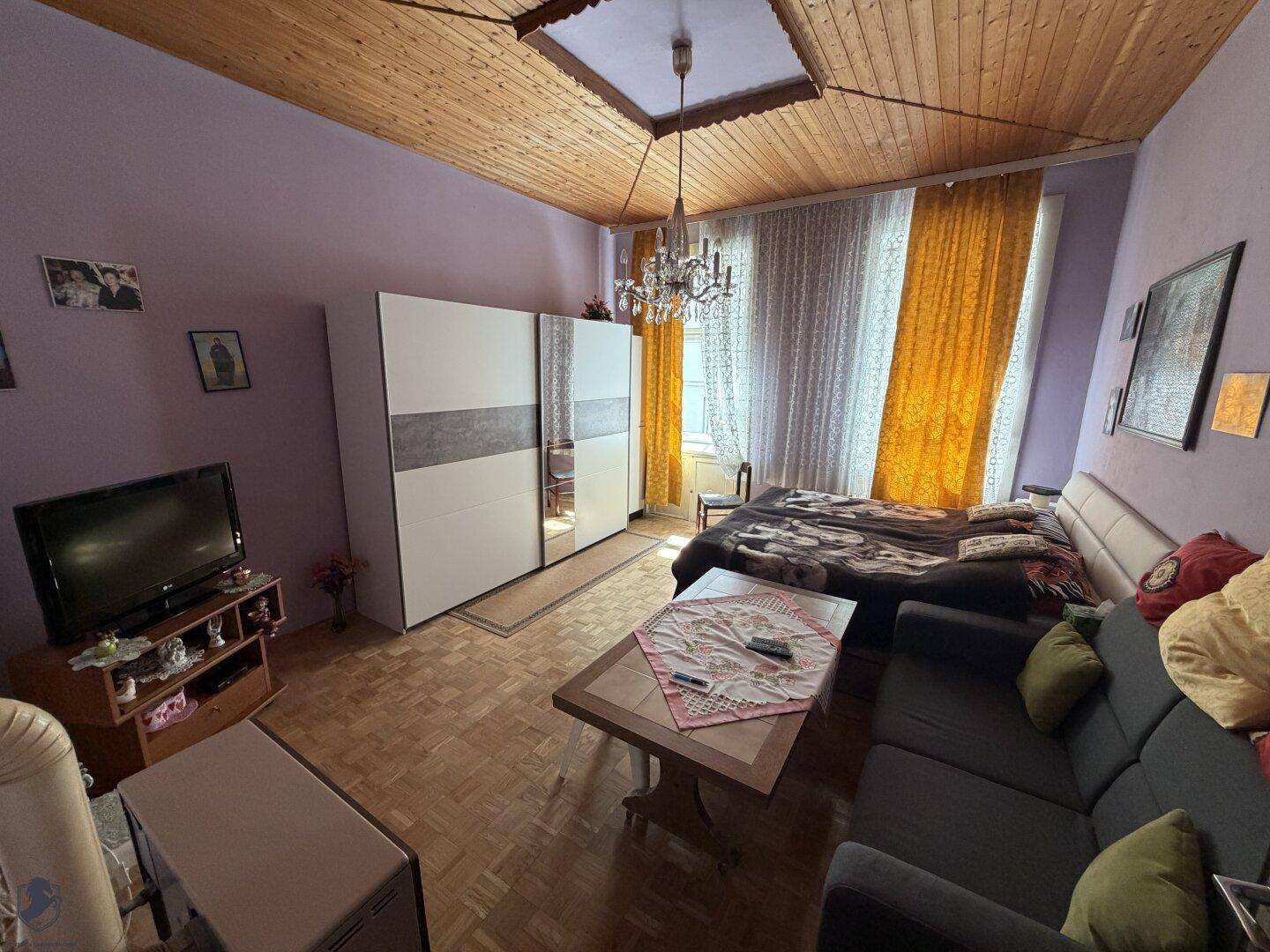 Wohn- und Schlafzimmer mit Holzbalkendecke, Parkettboden und einem großen Kleiderschrank.
