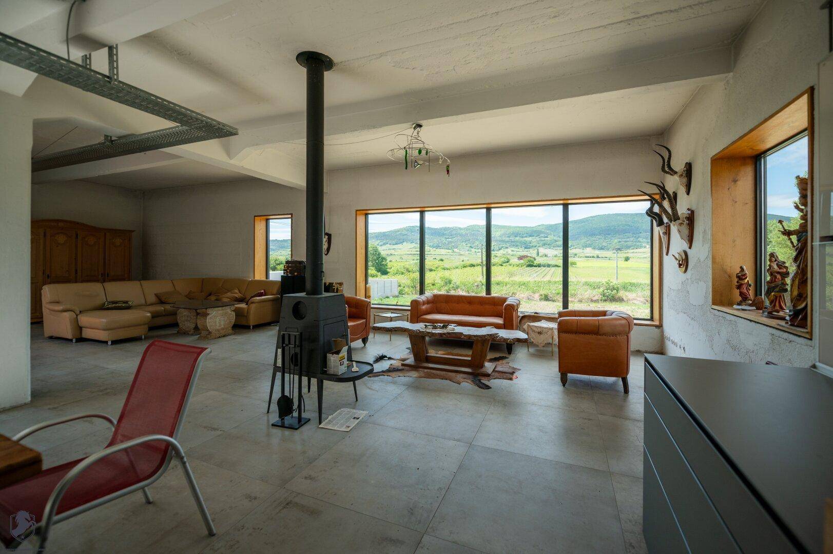 Geräumiges Wohnzimmer mit Kaminofen, Ledersofas und großen Fenstern mit weitem Blick ins Grüne.