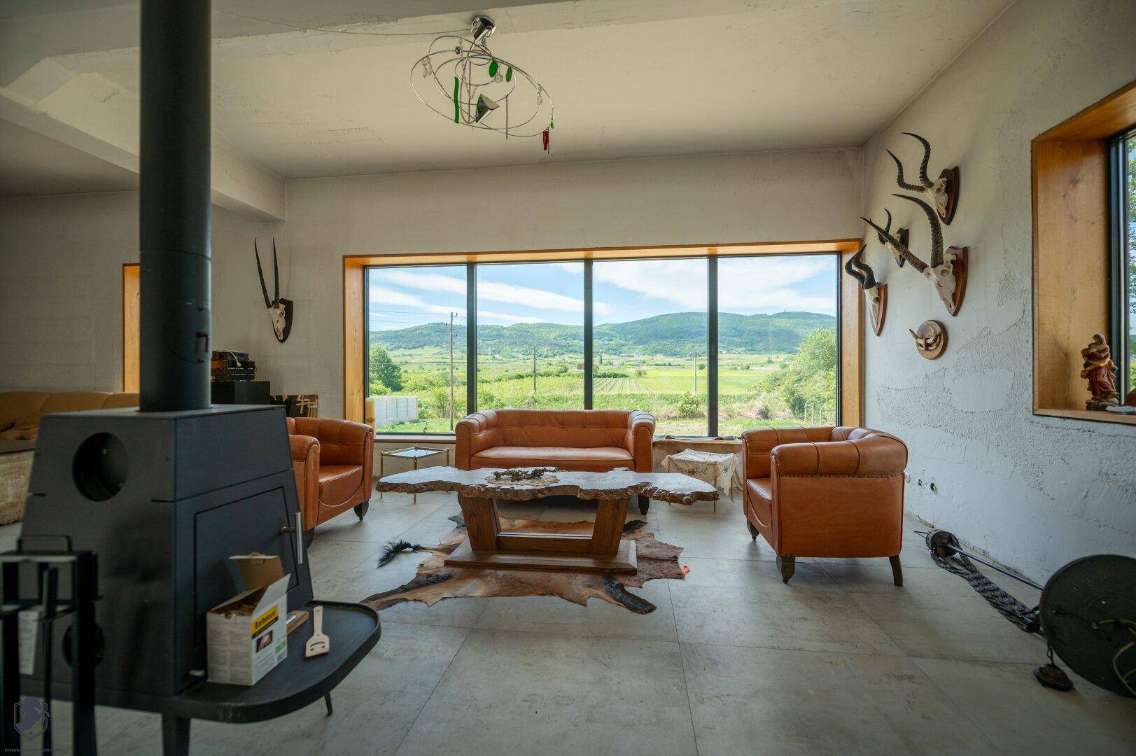 Gemütlicher Wohnbereich mit Kaminofen, Ledersesseln und Couch, umgeben von großen Fenstern mit Landschaftsblick.