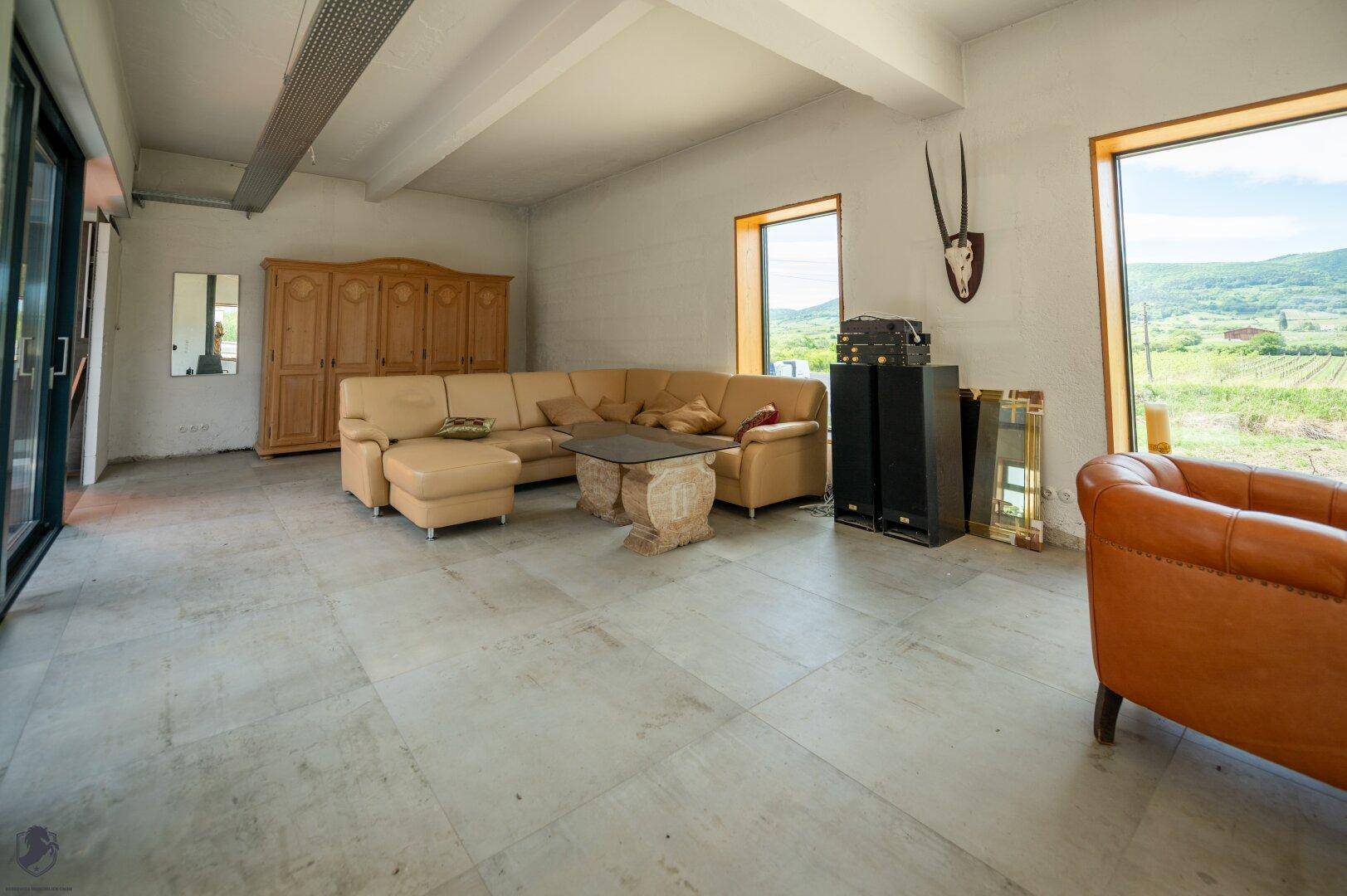 Heller Wohnbereich mit großem Ecksofa, Holzschrank und weitem Blick durch die Fenster in die Natur.