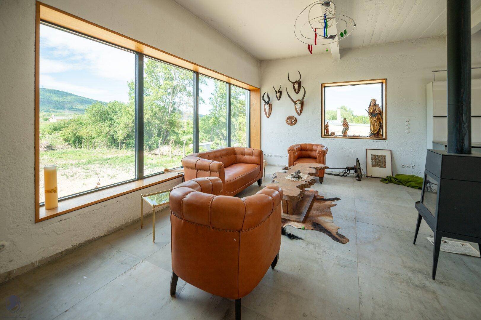 Gemütliche Ledersessel im Wohnzimmer mit großen Fenstern, die einen weiten Blick in die grüne Landschaft bieten.