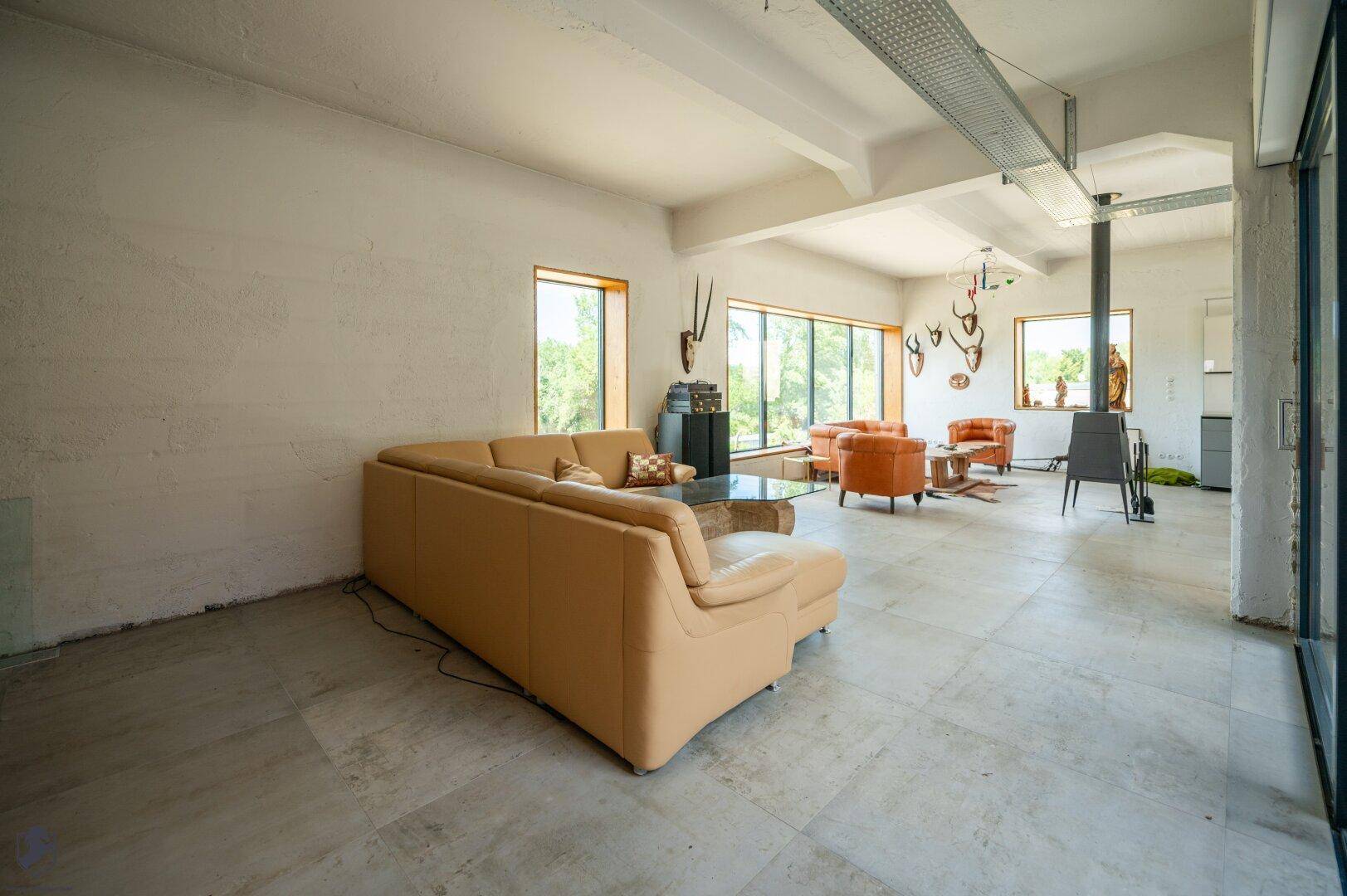 Großzügiger offener Wohn- und Essbereich mit Fliesenboden, Ledersofas und Blick auf die moderne Küche.