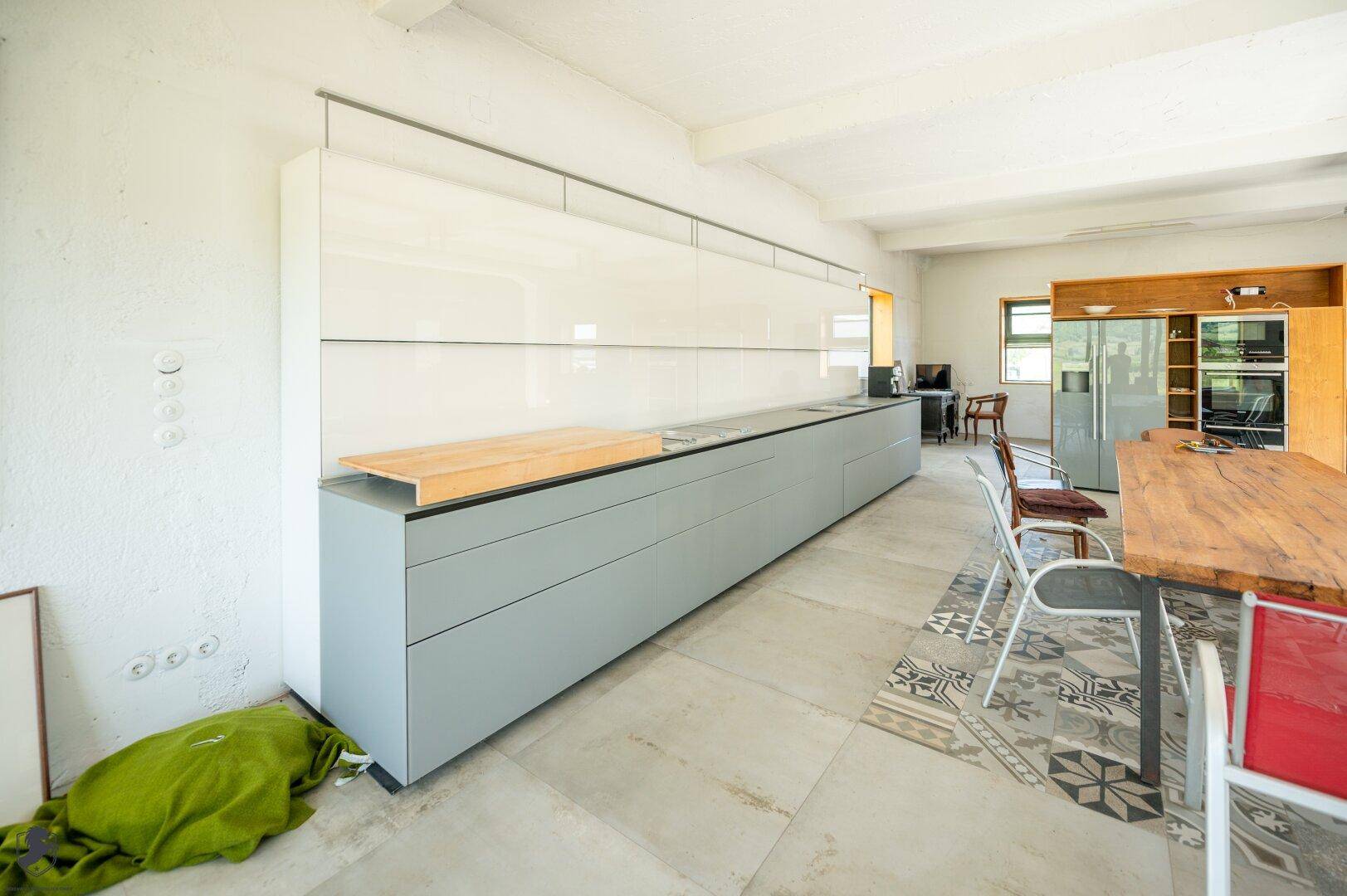 Moderne Küche mit langen, grauen Unterschränken, weißen Oberschränken und einem Holztisch im Essbereich.