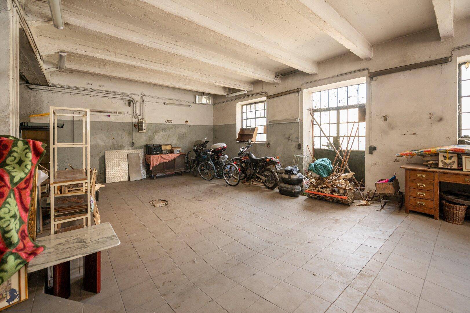 Weitläufiger Industrieraum mit hohen Decken, großen Fenstern und gelagerten Motorrädern.