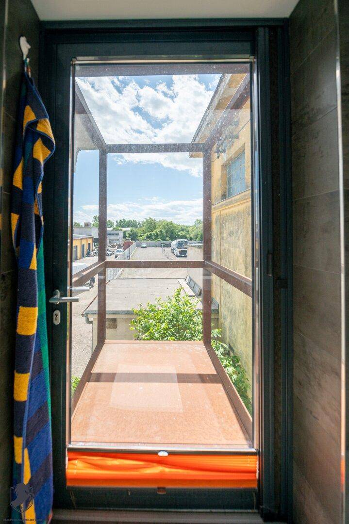Blick aus einem Innenraum durch eine Tür auf einen kleinen Außenbereich und die umliegenden Gebäude.