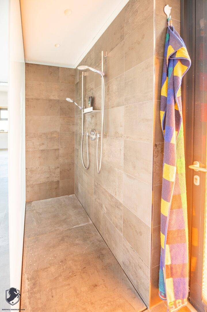 Moderne begehbare Dusche mit großformatigen Fliesen und farbenfrohem Handtuch am Türrahmen.