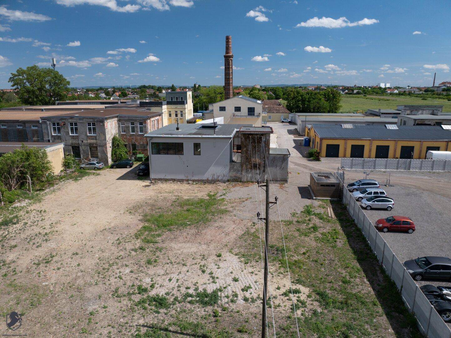 Panoramablick aus der Luft auf ein Industriegebiet mit freiem Grundstück und einem markanten Schornstein.