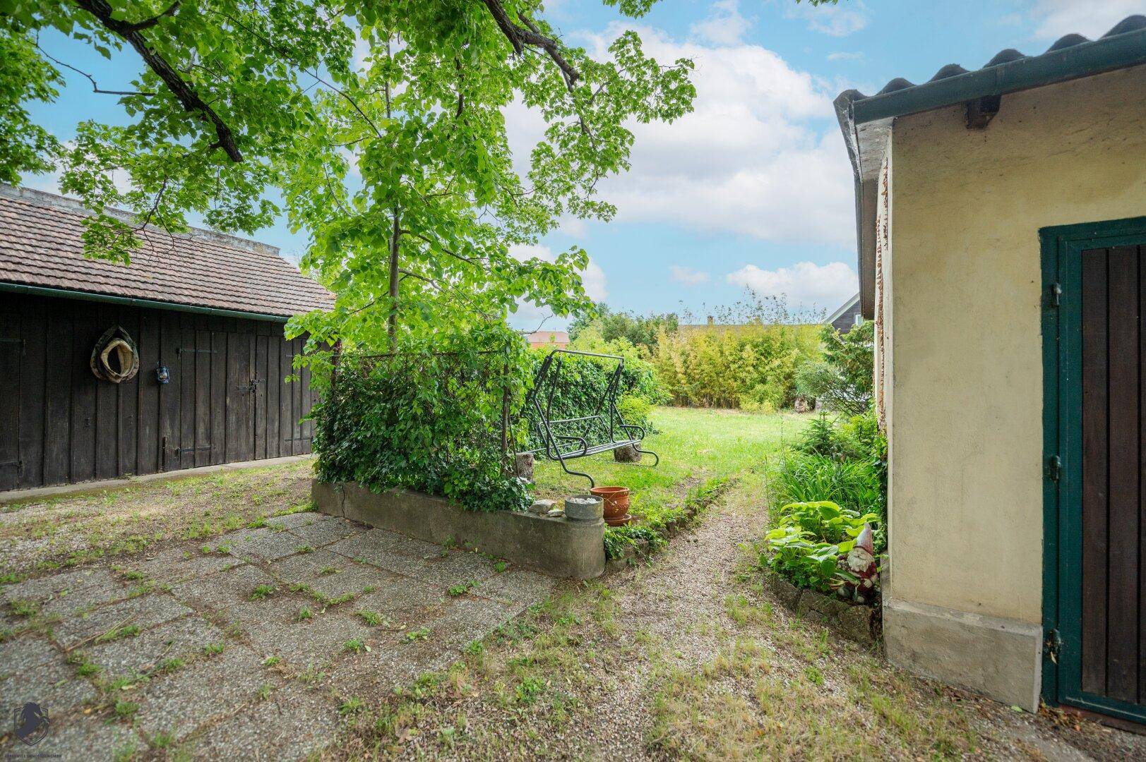 Teil des Gartens mit einer gepflasterten Fläche, einer Schaukel und üppigem Grün im Hintergrund.