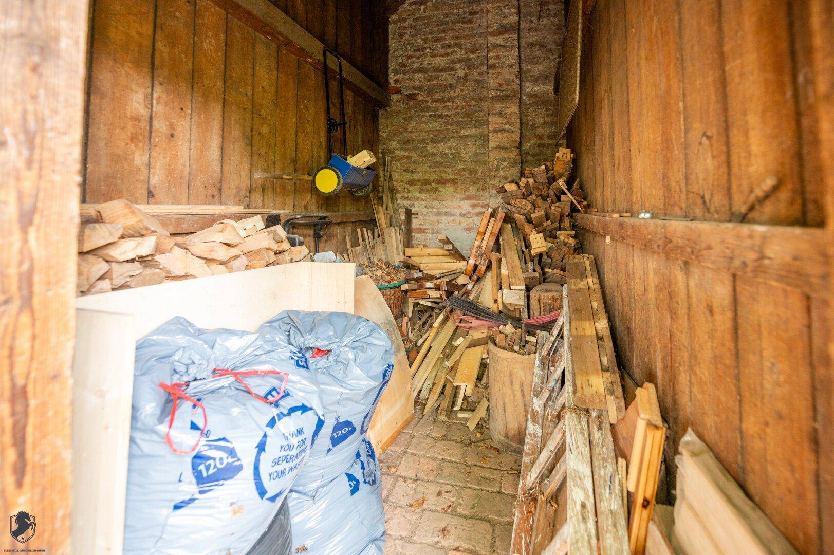 Lagerraum mit gestapeltem Brennholz und Baumaterialien, ideal für die Vorratshaltung.
