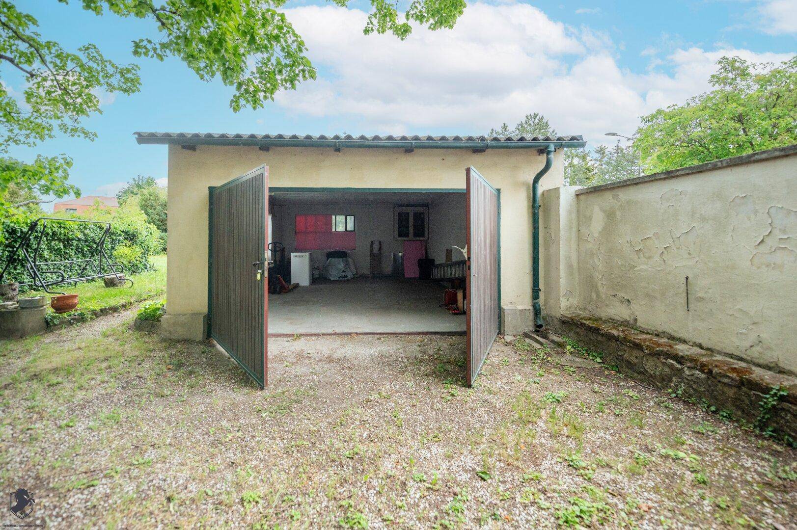 Offene Garage mit Holztoren, bietet Platz für Fahrzeuge und zusätzlichen Stauraum.