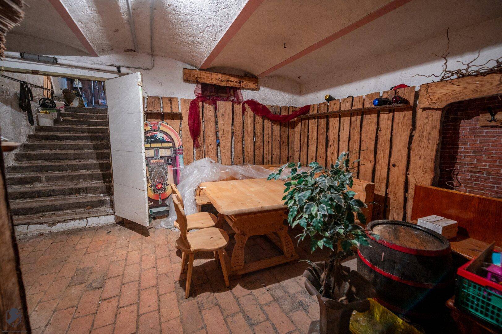 Rustikal eingerichteter Kellerraum mit Holztisch, Bänken und einer Jukebox, ideal für Feiern.