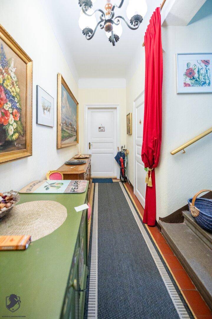 Langer Flur mit Teppichläufer, Kunstwerken an den Wänden und einer Treppe.