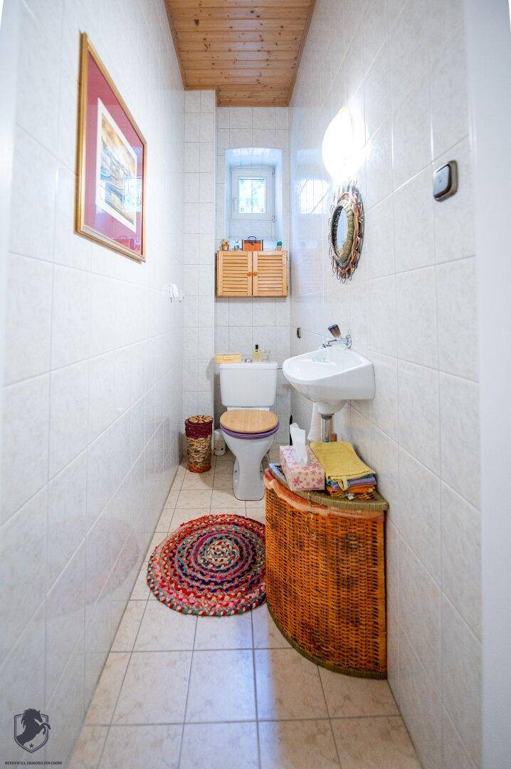 Kleines Gäste-WC mit weißen Fliesen, Holzdecke und einem Fenster.