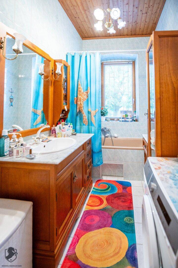 Buntes Badezimmer mit Badewanne, Waschbecken und Holzmöbeln unter einer Holzdecke.