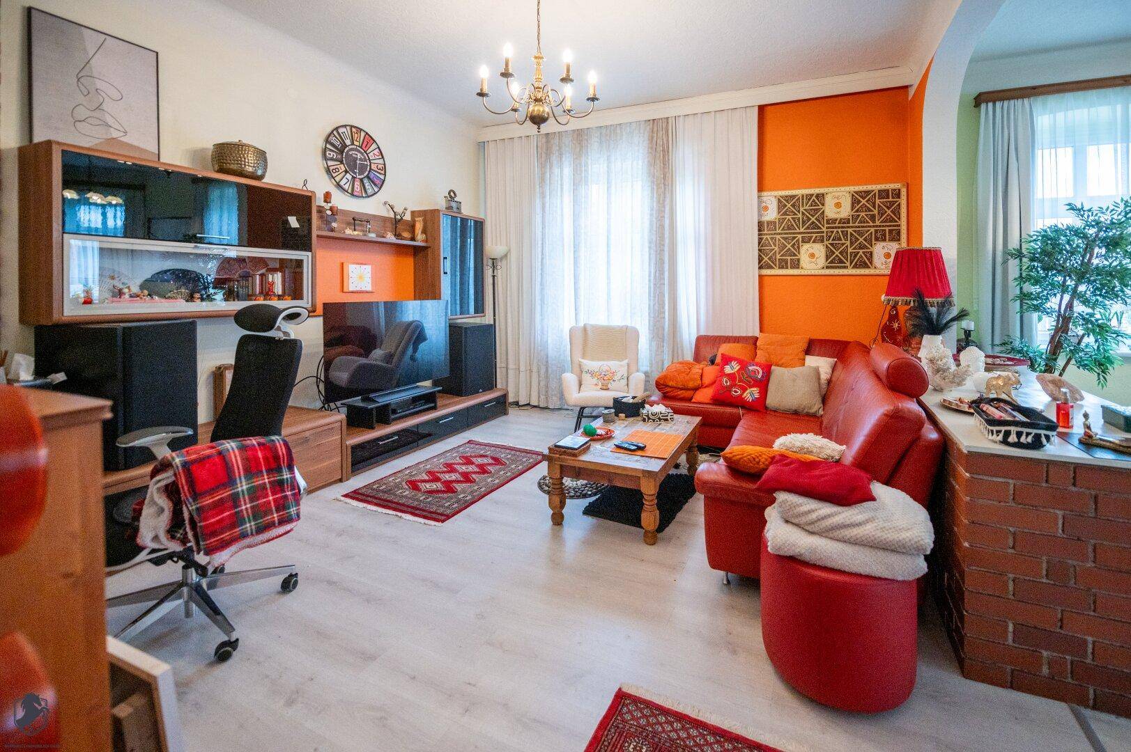 Geräumiges Wohnzimmer mit orangefarbenen Akzentwänden, rotem Sofa und hellem Boden.