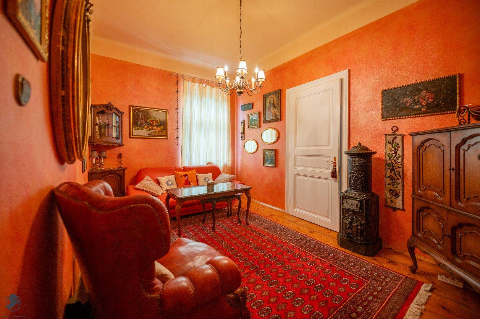 Gemütliches Wohnzimmer mit orangefarbenen Wänden, Holzboden und traditionellem Ofen.