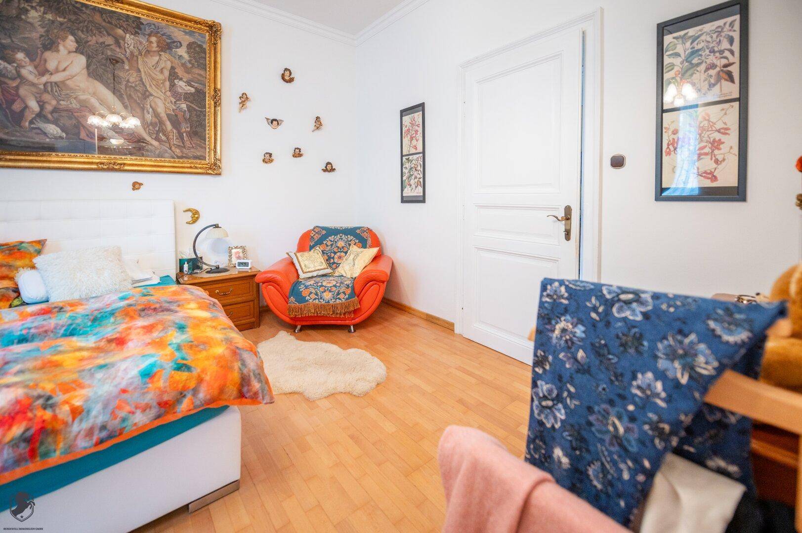 Helles Schlafzimmer mit Holzboden, farbenfroher Bettwäsche und großem Kunstwerk.