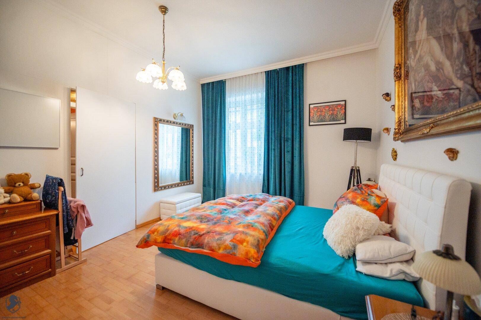Schlafzimmer mit Doppelbett, Holzboden, blauen Vorhängen und großem Spiegel.