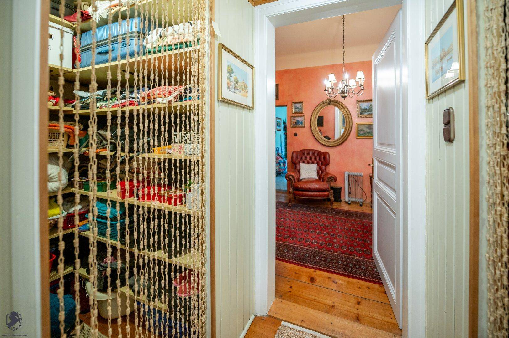 Flur mit offenem Kleiderschrank, Holzboden und Blick in ein Wohnzimmer.