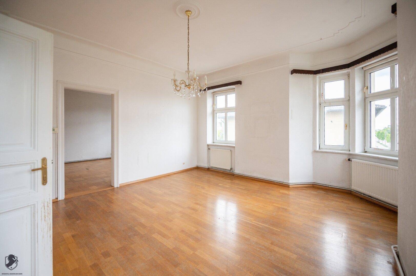 Helles Wohnzimmer mit Fischgrätparkett, Erkerfenstern und klassischem Kronleuchter.