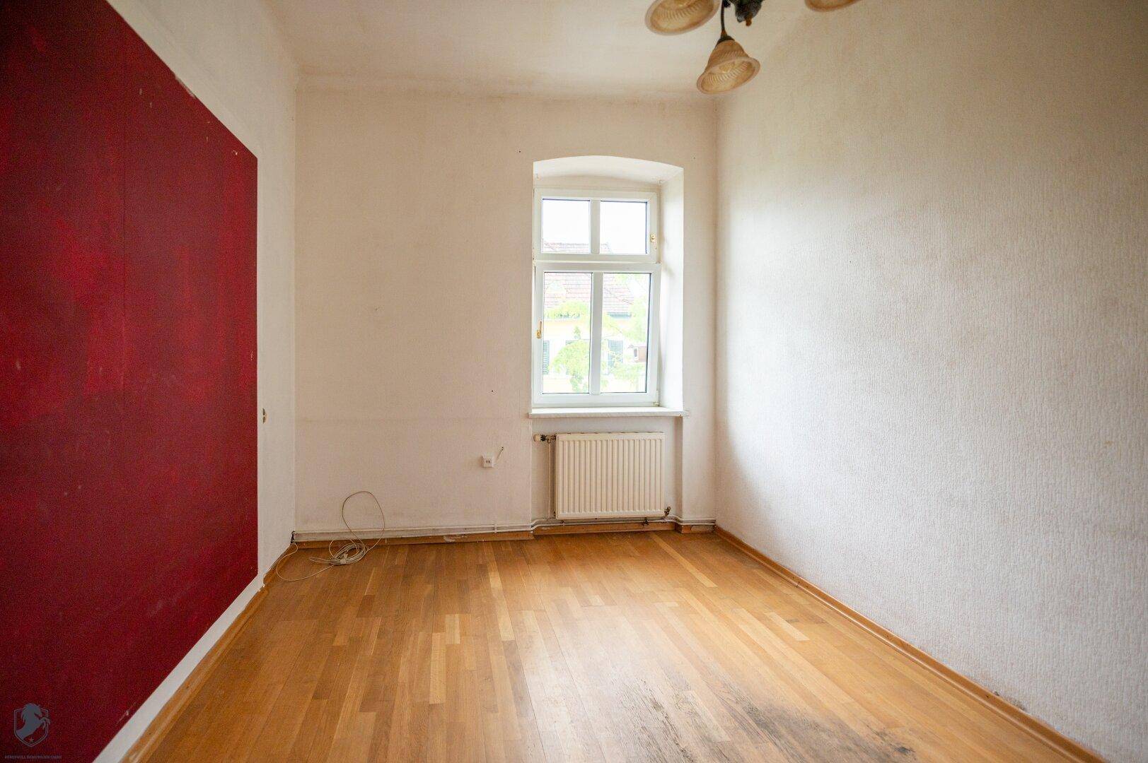 Helles Zimmer mit Parkettboden und einer auffälligen roten Akzentwand.