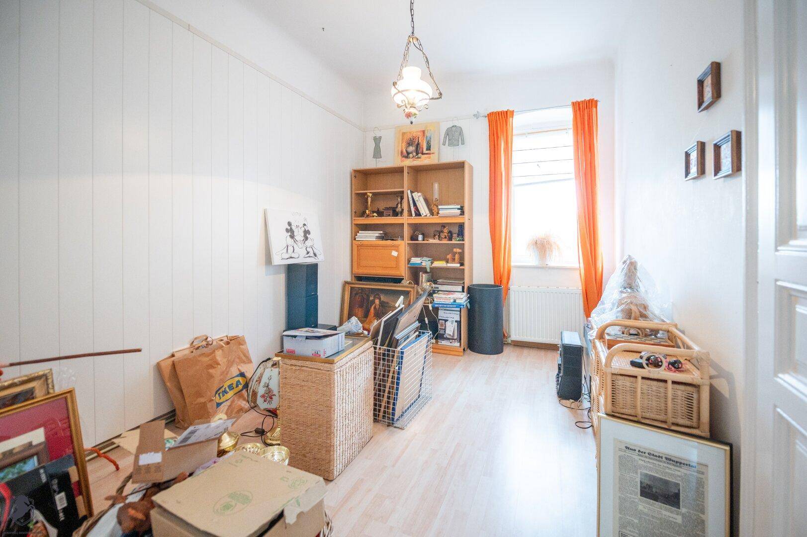 Helles Zimmer mit Laminatboden, Fenster und Bücherregal, derzeit als Abstellraum genutzt.