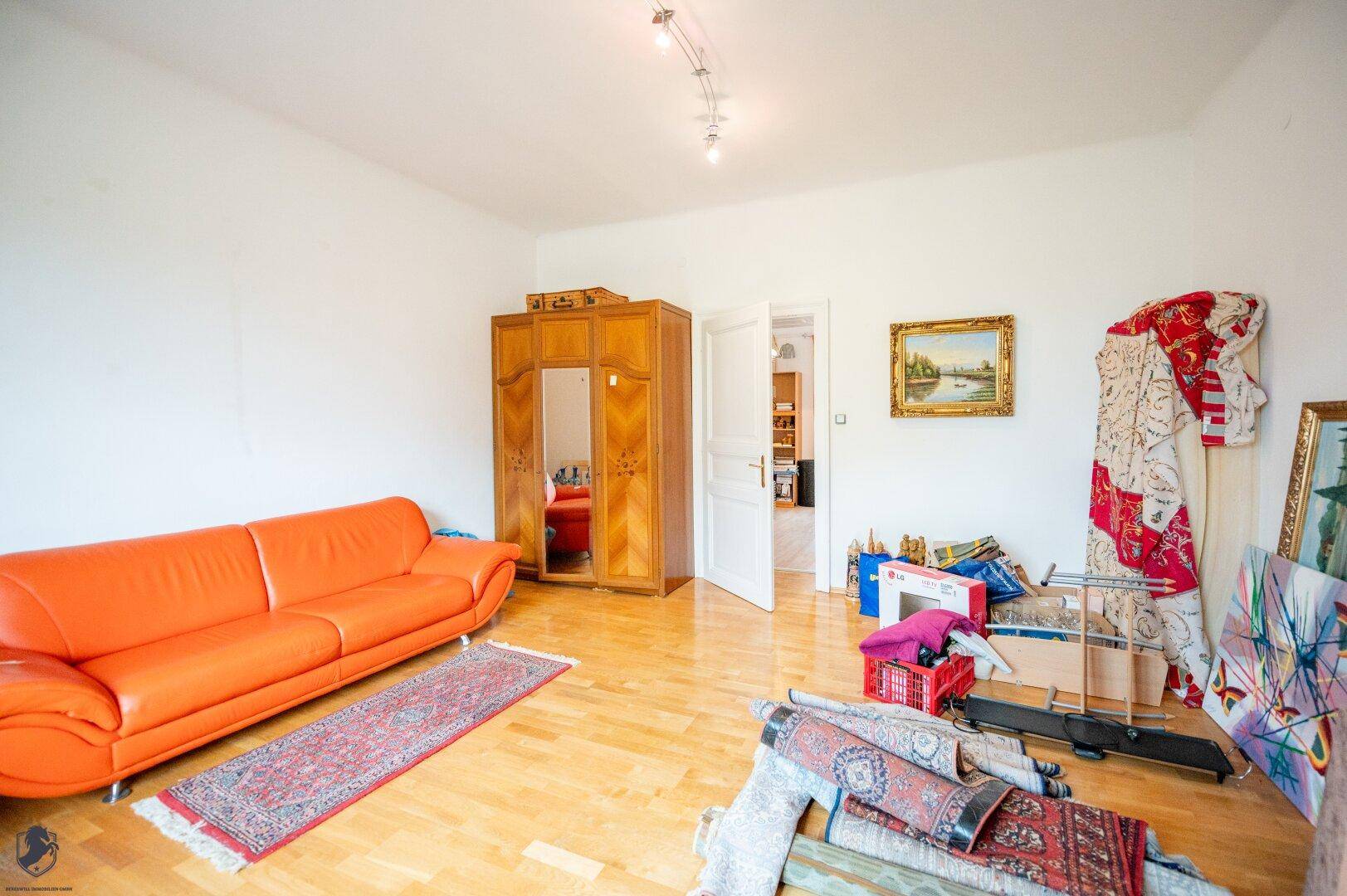 Wohnzimmer mit Parkettboden, orangefarbenem Sofa und klassischem Kleiderschrank.