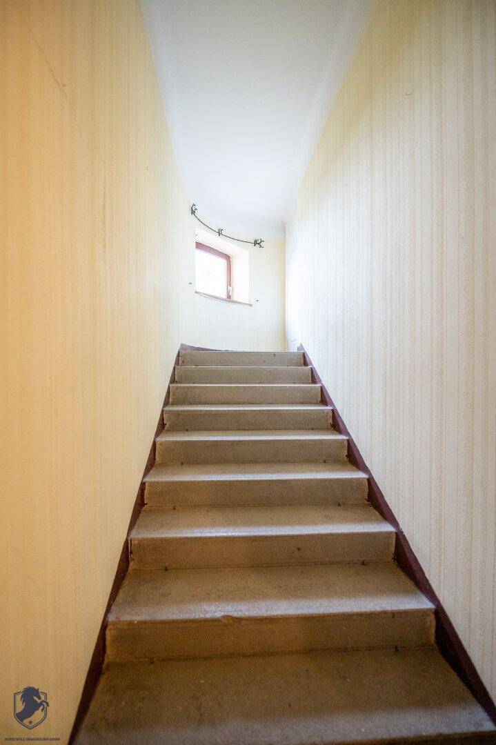 Treppenhaus mit heller Tapete und Fenster, das zu den oberen Etagen führt.