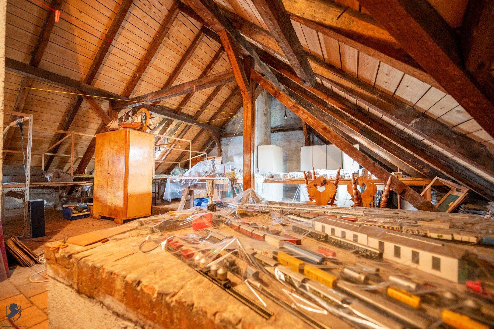 Geräumiger Dachboden mit sichtbaren Holzbalken und einer Modelleisenbahnanlage.