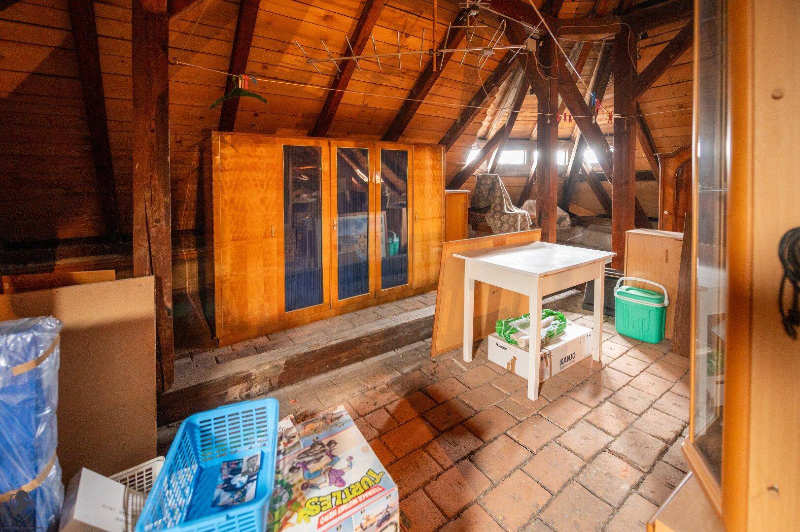 Dachboden mit Holzbalken, Terrakotta-Fliesenboden und Fenster, als Lagerraum genutzt.