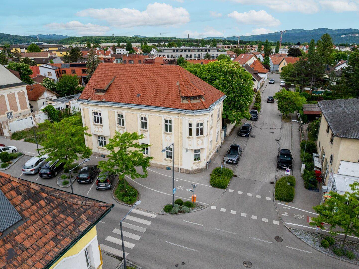 Panoramablick von oben auf ein historisches Gebäude an einer belebten Kreuzung mit parkenden Autos.